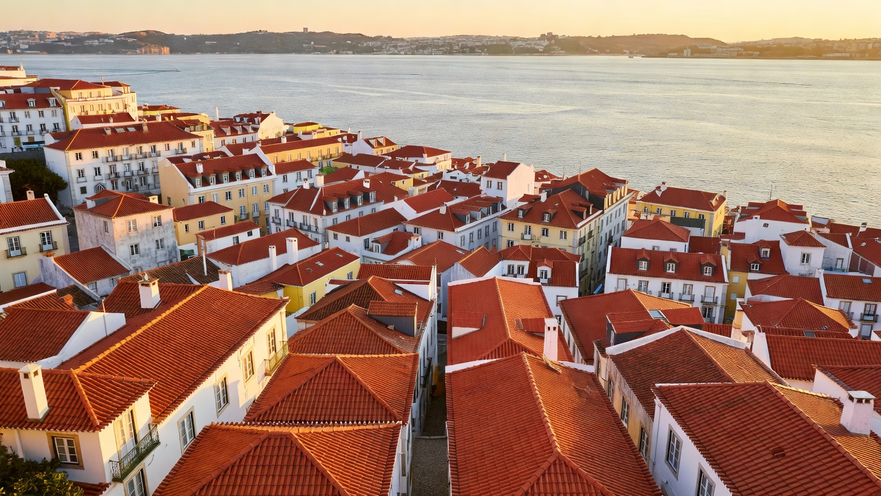 Terracotta rooftops of Lisbon's Alfama district stepping down towards the wide Tejo estuary in afternoon light